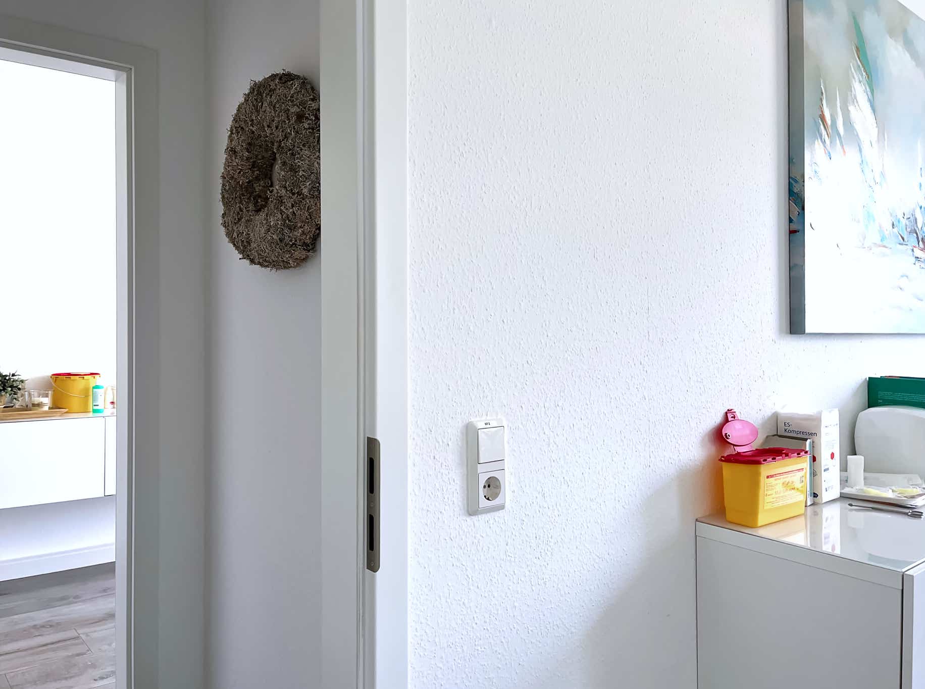 weitlaeufig wirkender blick von einem behandlungsraum ueber den flur zum naechsten praxiszimmer aus stafiert mit unaufdringlicher dekoration