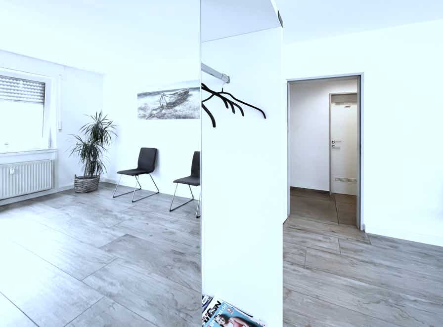 helles, sonniges ambiente im wartezimmer mit garderobe, stuehlen und blick in den flur
