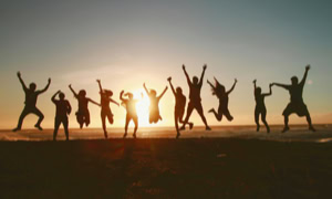 Silhouetten von Menschen, die bei Sonnenuntergang am Strand in die Luft springen.