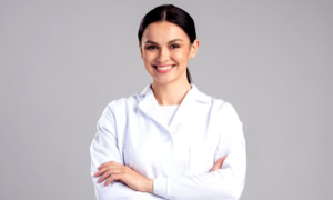 Frau in weißem Laborkittel mit verschränkten Armen vor grauem Hintergrund.