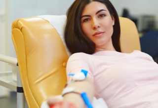 Eine Person sitzt auf einem gelben Stuhl und spendet Blut, mit einem Verband am Arm.