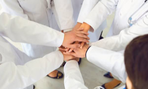 Mehrere Personen in weißen Kitteln legen ihre Hände übereinander in der Mitte.