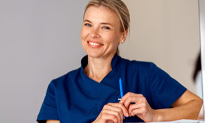 Eine lächelnde Person in blauer Arbeitskleidung hält einen Stift in der Hand.