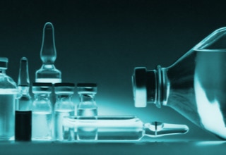 Verschiedene Glasfläschchen und Ampullen auf einem Tisch, mit einer großen liegenden Flasche rechts.