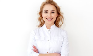 Frau mit lockigem Haar in weißem Hemd lächelt mit verschränkten Armen vor weißem Hintergrund.