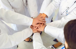 Mehrere Personen in weißen Kitteln legen ihre Hände übereinander in der Mitte eines Kreises.