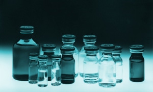 Mehrere Glasfläschchen mit Flüssigkeit, auf einem beleuchteten Hintergrund angeordnet.