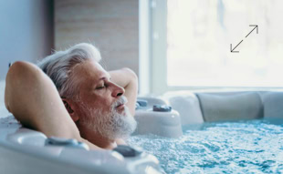 &Auml;lterer Mann mit grauem Haar und Bart entspannt sich in einem Whirlpool, mit geschlossenen Augen und H&auml;nden hinter dem Kopf.