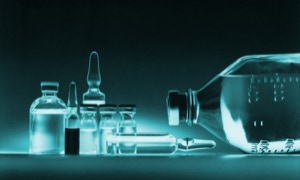 Verschiedene Glasfläschchen und Ampullen auf einer Oberfläche, mit einer großen liegenden Flasche rechts.