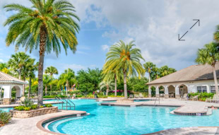 Ein Au&szlig;enpool mit Palmen, umgeben von Geb&auml;uden mit wei&szlig;en W&auml;nden und grauen D&auml;chern unter einem bew&ouml;lkten Himmel.