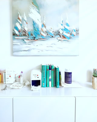 weisses sideboard mit fachbuechern und anderen nessecaires, darueber ein grossformatiges gemaelde mit stilisierten segelbooten