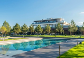 Ein rechteckiger Pool vor einem modernen Gebäude, umgeben von grünen Rasenflächen und Bäumen unter klarem Himmel.