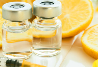 Zwei Glasfl&auml;schchen mit Fl&uuml;ssigkeit, umgeben von aufgeschnittenen Zitronen und einer Spritze.