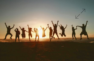 Silhouetten von Menschen, die bei Sonnenuntergang am Strand in die Luft springen.