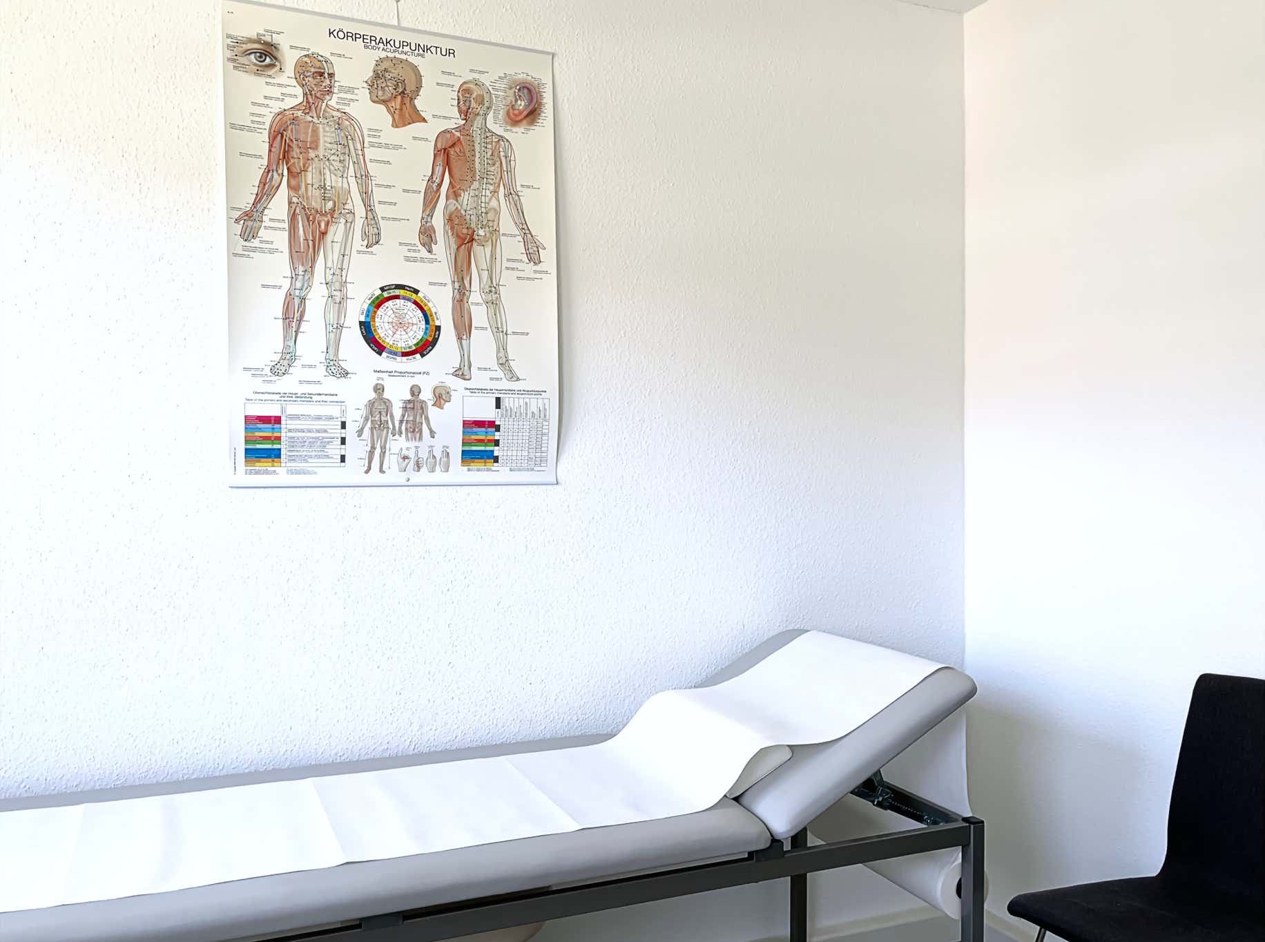 heller untersuchungsraum mit patientenliege und akupunktur poster an der weissen wand