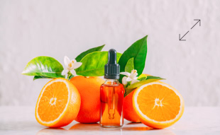 Orangen und eine Flasche mit Pipette, umgeben von gr&uuml;nen Bl&auml;ttern und wei&szlig;en Bl&uuml;ten, auf hellem Hintergrund.