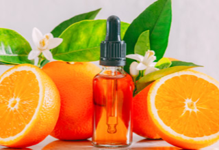 Eine Flasche mit Pipette steht zwischen zwei Orangenh&auml;lften und einer ganzen Orange, umgeben von gr&uuml;nen Bl&auml;ttern.