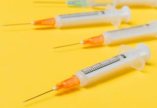 Vier Spritzen mit orangefarbenen Spitzen liegen auf einem gelben Hintergrund.