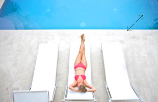 Person in rotem Badeanzug liegt auf einer Sonnenliege neben einem Pool, umgeben von zwei leeren Liegen.