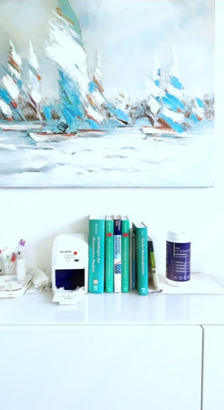 weisses sideboard mit fachbuechern und anderen nessecaires, darueber ein grossformatiges gemaelde mit stilisierten segelbooten