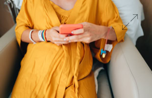Person in gelbem Gewand sitzt auf einem Sessel und hält ein rotes Smartphone in den Händen.