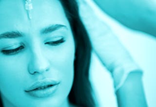 Frau mit geschlossenen Augen, Gesicht nach oben gerichtet, während eine behandschuhte Hand ihr Haar berührt.