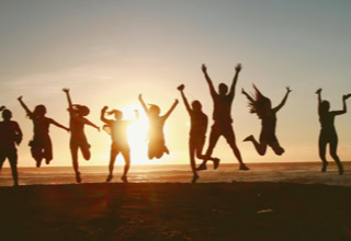 Gruppe von Menschen, die am Strand bei Sonnenuntergang in die Luft springen.