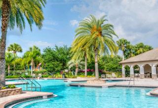 Ein Au&szlig;enpool mit Palmen, umgeben von Geb&auml;uden mit B&ouml;gen und einem bew&ouml;lkten Himmel im Hintergrund.