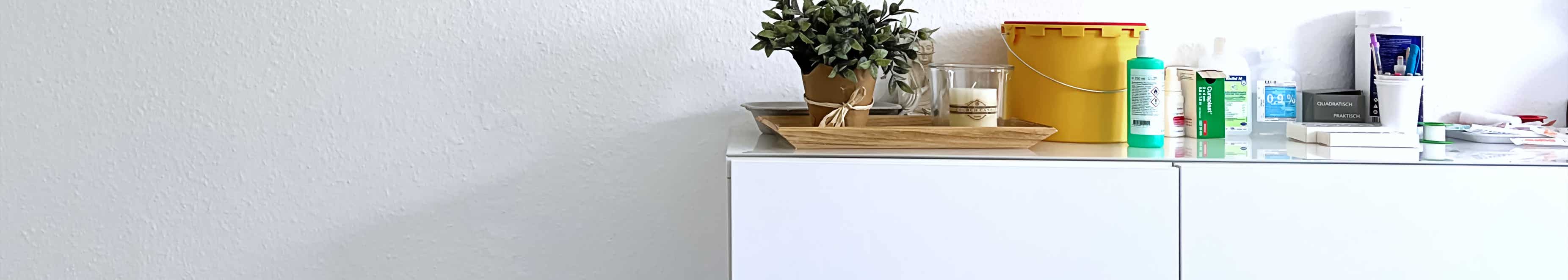 weisses sideboard mit fachbuechern und anderen nessecaires, darueber ein grossformatiges gemaelde mit stilisierten segelbooten
