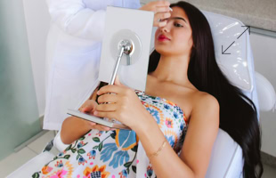 Frau liegt auf einem Stuhl, hält einen Spiegel und wird von einer Person in weißem Kittel behandelt.