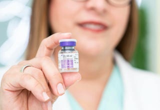 Eine Person hält ein kleines Fläschchen mit violettem Deckel in der Hand.